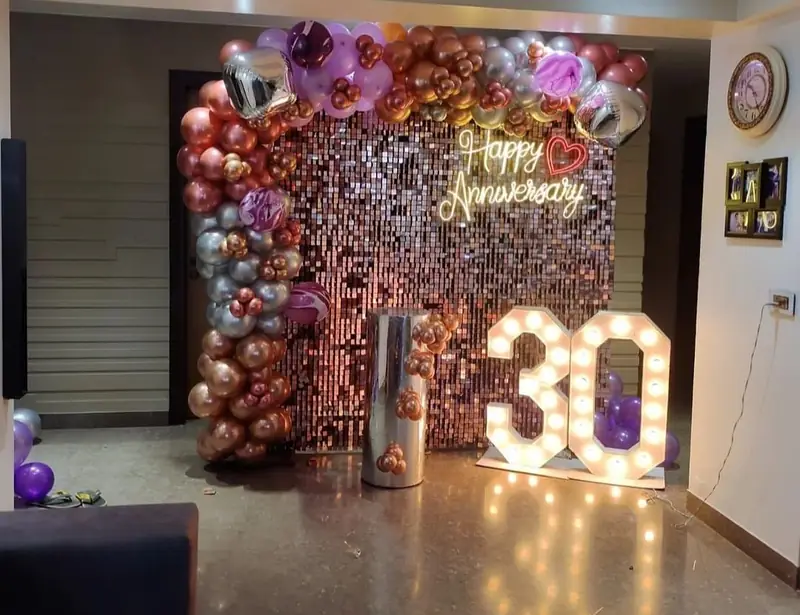 Rose gold sequin shimmer wall with a balloon garland and a lit 30 in bulb letters.