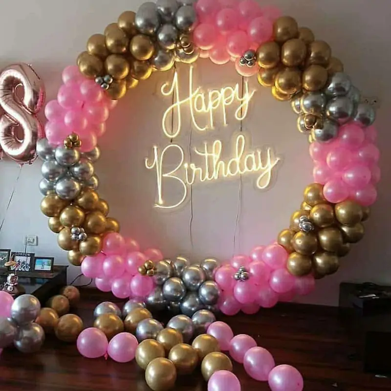 Pink, gold and silver balloon ring around a neon Happy Birthday sign with a large standing letter S.