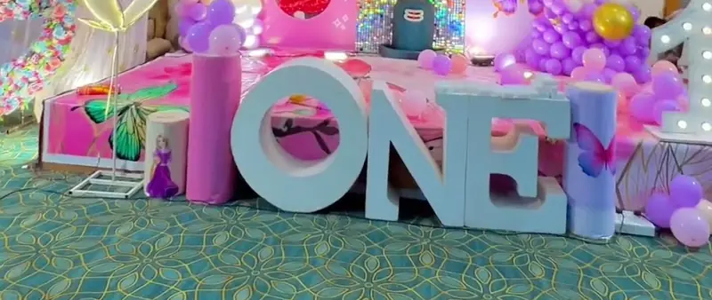 Large standing ONE letters in front of a lit backdrop with purple and pink balloons.