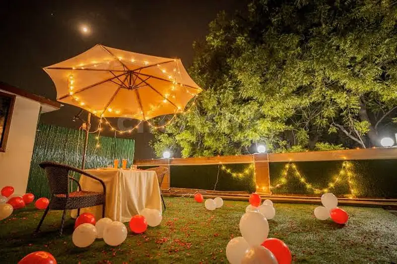 An evening garden setup with a lit umbrella over a small table and balloons on the lawn.
