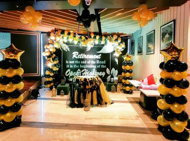A retirement party set up in an office with black and gold balloon columns and a lit board on the wall.